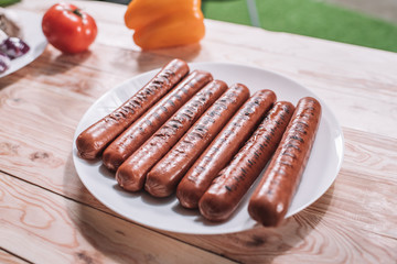 Close-up view of tasty fresh grilled sausages on white plate on wooden table