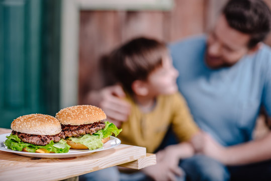 Close Up View Of Homemade Burgers On Plate With Family Behind