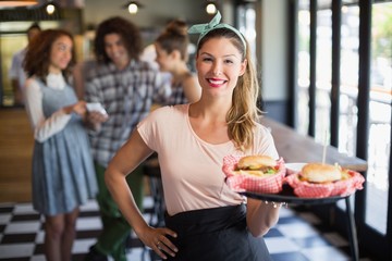 Smiling young waitress serving burger in restaurant