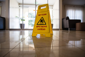 Sign showing warning of caution wet floor on wet tile floor in sunset