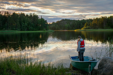 A fisherman stands in a boat on the lake, on the background of beautiful sunset sky and its reflection in the water