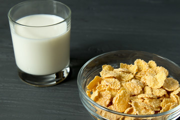Corn flakes on glass bowl and glass of milk isolated on grey surface