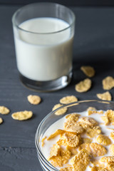 Glass of milk and cornflakes in a bowl on a grey surface