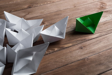 Business leadership concept with white and color paper boats on wooden table