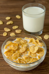 Corn flames in a bowl with milk and glass of milk on wooden surface