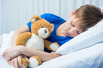 Obraz na płótnie Canvas Sick little boy sleeping in hospital bed with teddy bear