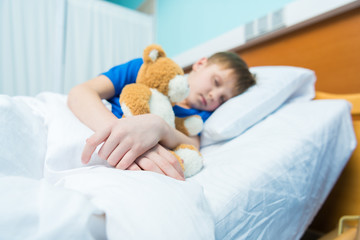 Sick little boy sleeping in hospital bed with teddy bear