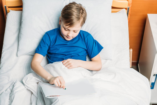 Smiling Little Boy Drawing While Lying In Hospital Bed