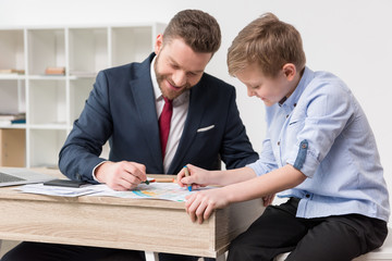 Businessman drawing on business papers with son at office