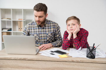 Businessman freelancer working at table with son at home office