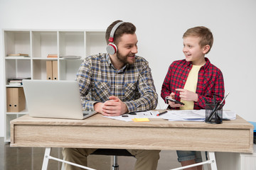 Businessman in headphones with son at office