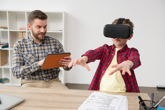 Businessman with boy wearing virtual reality glasses at home office