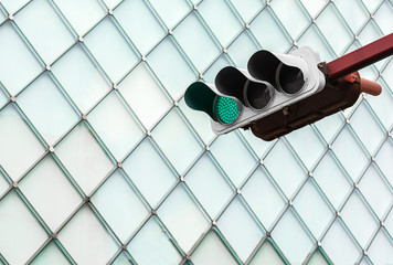 Green traffic light with glass windows of building in background.