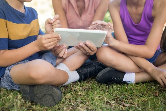 Grandmother And Grand Kids Using Digital Tablet In The Park