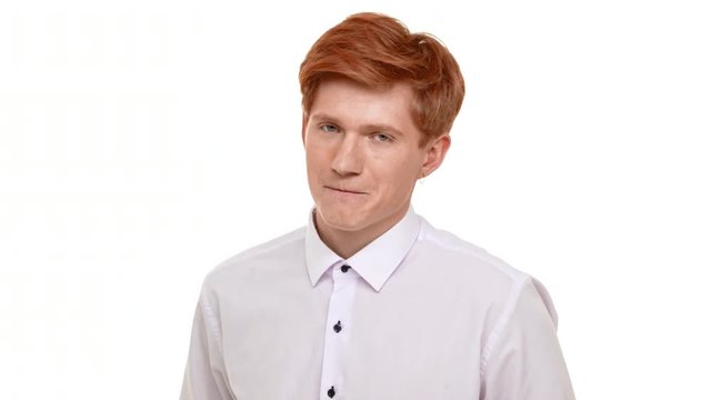 Shy handsome Caucasian foxy young man standing on white background looking at camera with embarrassment