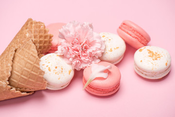 Closeup of macarons group with waffle cones and Carnation flower on pink surface. Macarons background concept