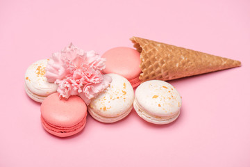 Closeup view of fresh macarons with waffle cones and Carnation flower on pink background. Sweets background concept