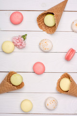 Variety of fresh macaroons in waffle cones on wooden surface. Colorful macarons pattern concept