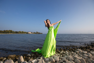 Portrait Cute brunette on the beach in a green dress, at the sea in sunny light weather