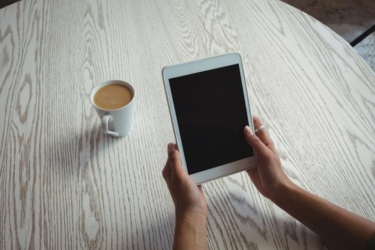 Hands of woman holding digital tablet by coffee 
