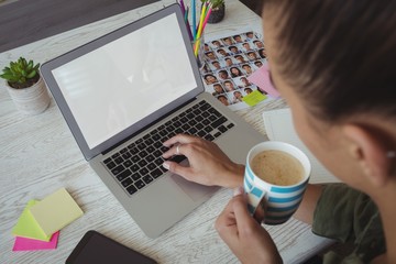 Female holding coffee cup while using laptop