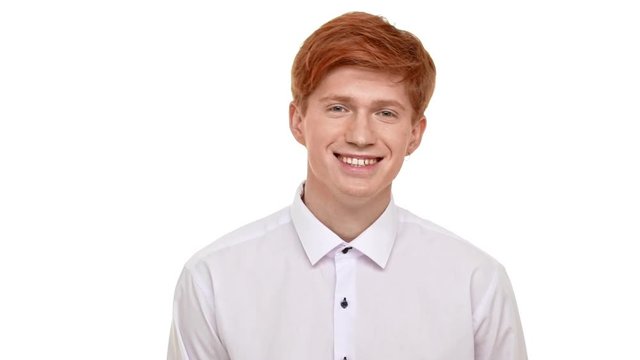 Handsome Caucasian young man with ginger hair standing on white background and smiling in slowmotion