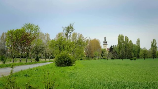 Picturesque landscape with a chapel in the background and golden wheat field in the foreground. Smal church in sunny idyllic landscape with positive atmosphere. Static day stabilized shot.