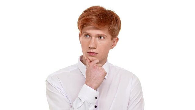 Thoughtfull Caucasian young boy with ginger hair standing on white background and holding his chin. Footage in slowmotion
