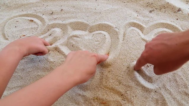 Closeup of tanned human hands of family of three persons. Father, mother and little son drawing heart shapes in sand on river beach. Love and togetherness concept. Real time full hd video footage.