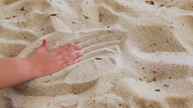 Closeup of little child hand drawing heart shape with his fingers in sandy beach background. Real time full hd video footage.