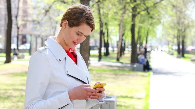 SMS. Young beautiful woman reads messages on cellphone sitting on bench in park