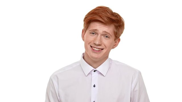 Shy handsome Caucasian foxy young man standing on white background looking at camera with embarrassment in slowmotion