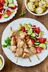 Chicken kebab and fresh vegetable salad,young potatoes on a wooden background, top view