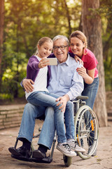 family selfie time- granddaughter, daughter and disabled man in wheelchair .