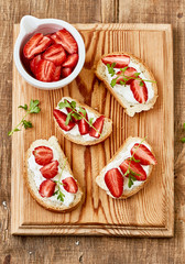 Canape with cottage cheese and strawberry on a cutting board, top view