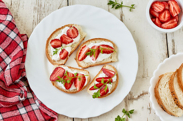 Small canape, crostini with cream cheese and strawberry on white plate.Top view. Flat lay