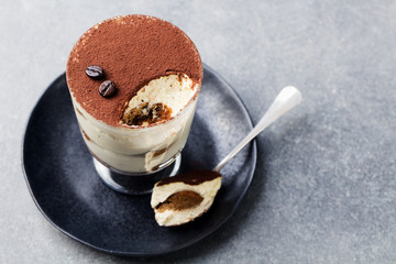 Tiramisu, traditional Italian dessert in glass on a grey stone background. Copy space.