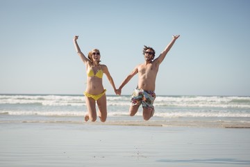 Cheerful couple holding hands while jumping at beach
