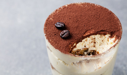 Tiramisu, traditional Italian dessert in glass on a grey stone background. Copy space