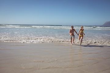 Full length of couple running on shore at beach