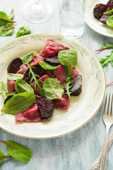 Homemade pink ravioli (tortellini) with goat cheese decorated beet leaves, beetroot slices and cranberry on wooden table. Selective focus