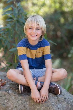 Smiling little boy sitting on rock in forest