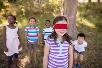 Fototapeta premium Friends looking at blindfolded girl standing in forest