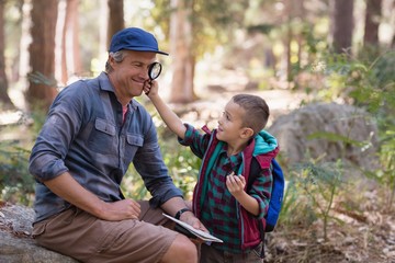 Boy showing magnifying glass to father while hiking in forest