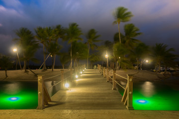 Wooden bridge at Camana Bay spanning over the Caribbean Sea leading to a sandy tropical beach illuminated by lanterns on a windy night, Grand Cayman , Cayman Islands