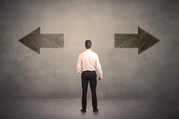 Business man taking a decision while standing in front of two grungy arrows on wall