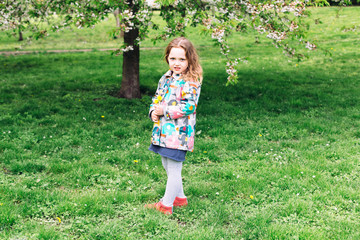 Cute smiling little girl  playing in spring blossoming garden. Kid plays outdoors.