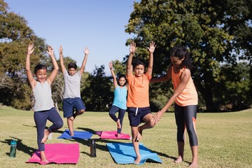 Naklejka premium Trainer examining kids practicing yoga