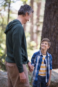 Smiling boy and father looking at each other in forest