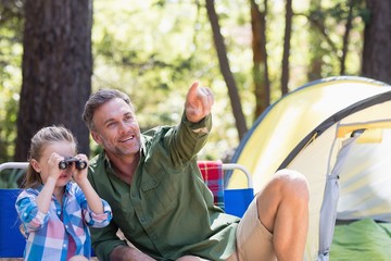 Daughter using binoculars with father in forest